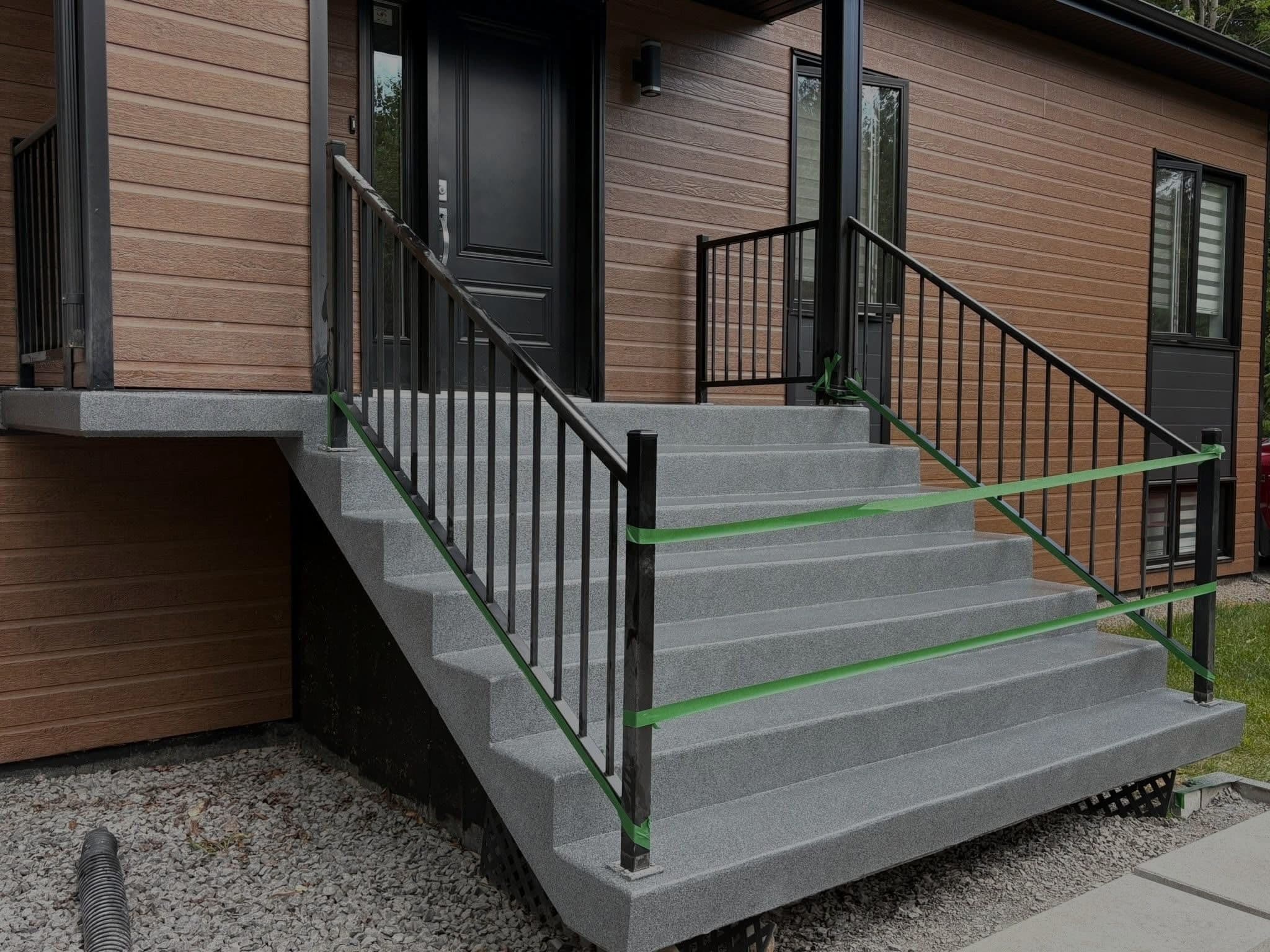 Escalier extérieur en béton recouvert d'un fini gris antidérapant, devant une maison récente